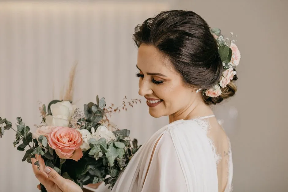 A bride in a white dress holding a bouquet, smiling with an elegant updo hairstyle.