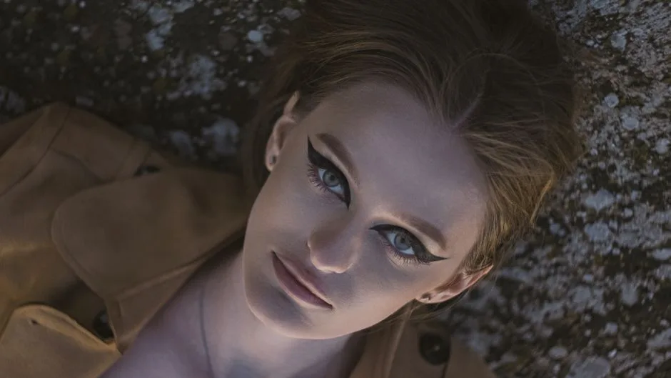 Close-up portrait of a woman lying outdoors with bold eyeliner makeup, showcasing dramatic beauty.