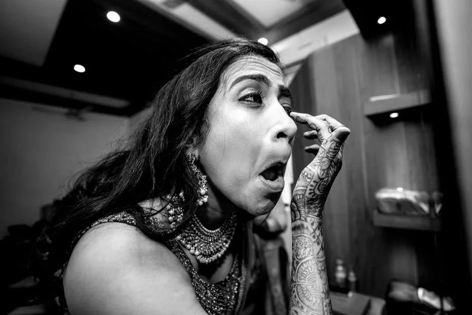 A bride carefully applies makeup in preparation for her wedding day, showcasing intricate mehndi and traditional jewelry.