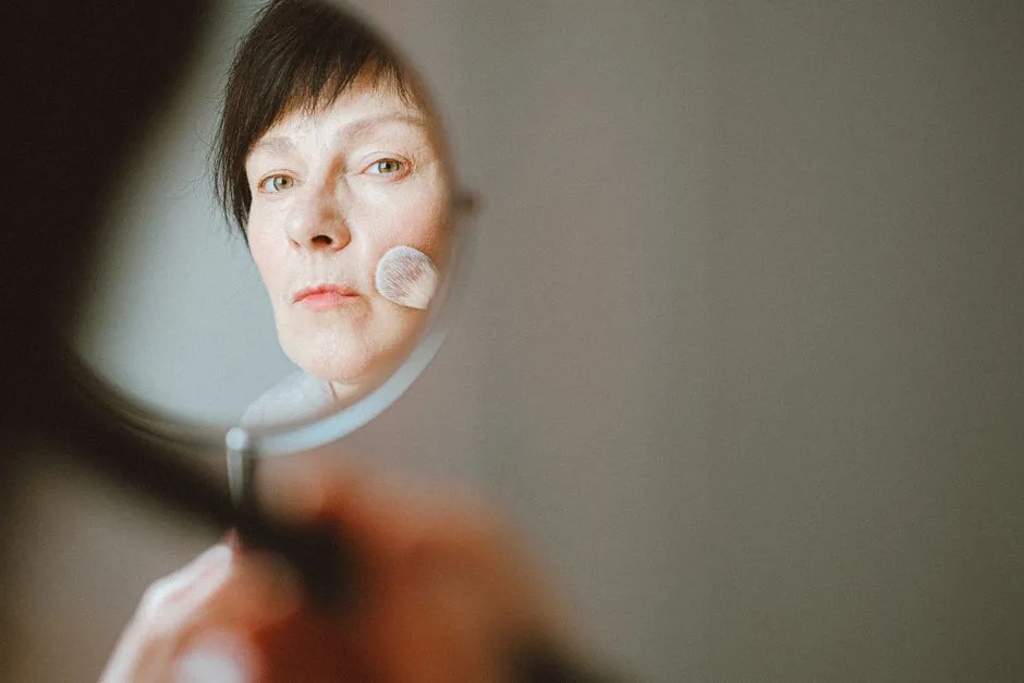 A senior woman applies makeup in a mirror, highlighting aging beauty.